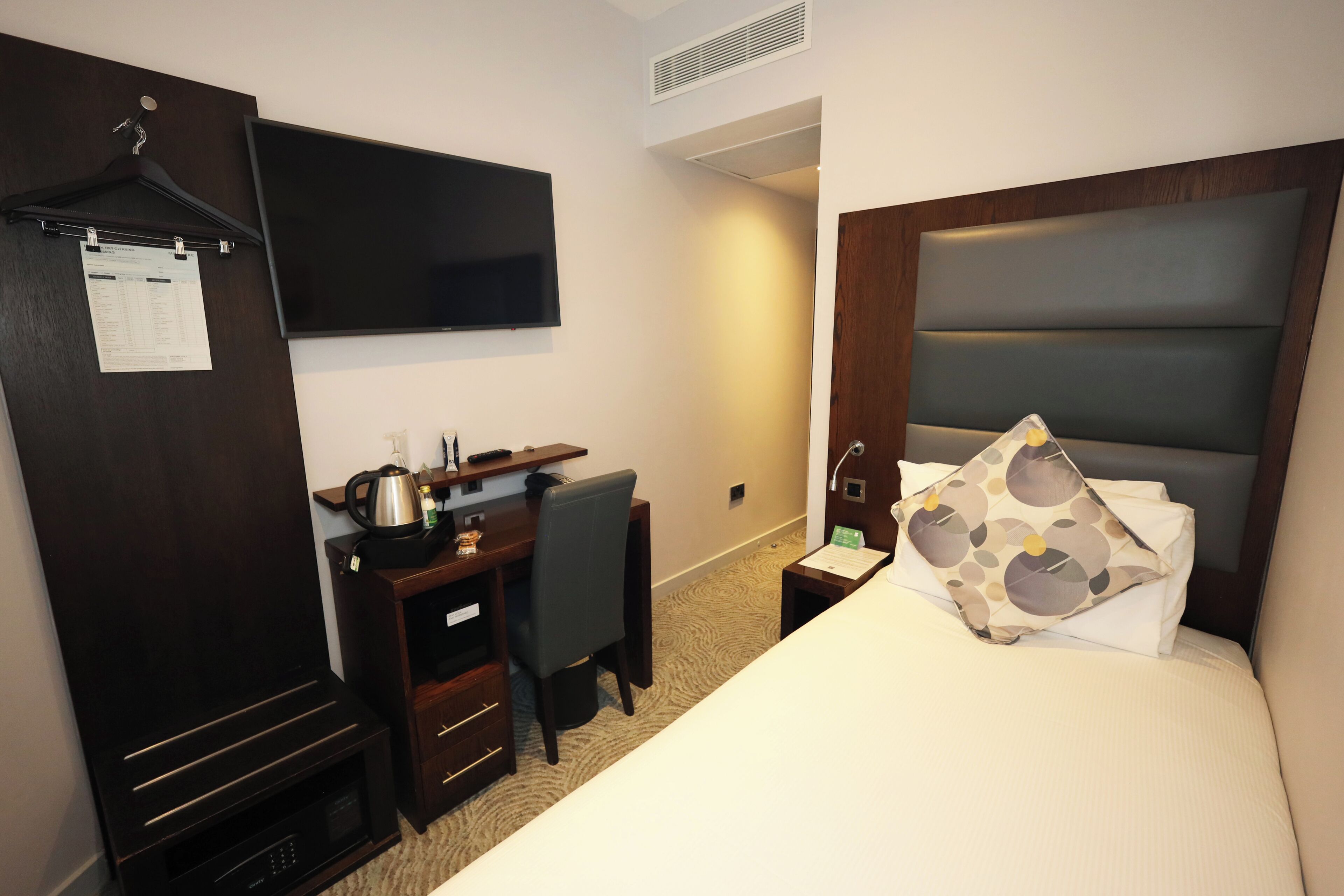 A hotel room with a bed, a desk, a chair, a television, and a coat rack.