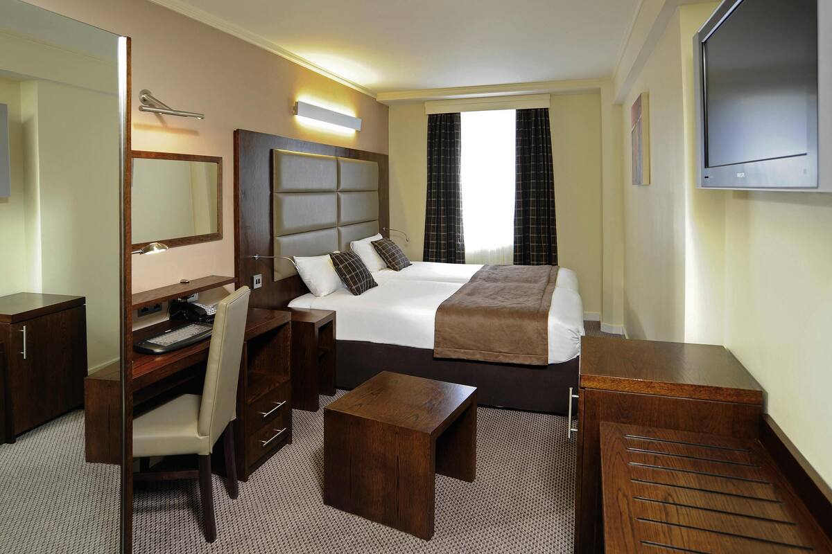A hotel room with a bed, desk, chair, and a television.