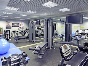 Une salle de sport équipée de divers appareils d’exercice, d’un grand ballon bleu et d’un écran de télévision fixé au mur.