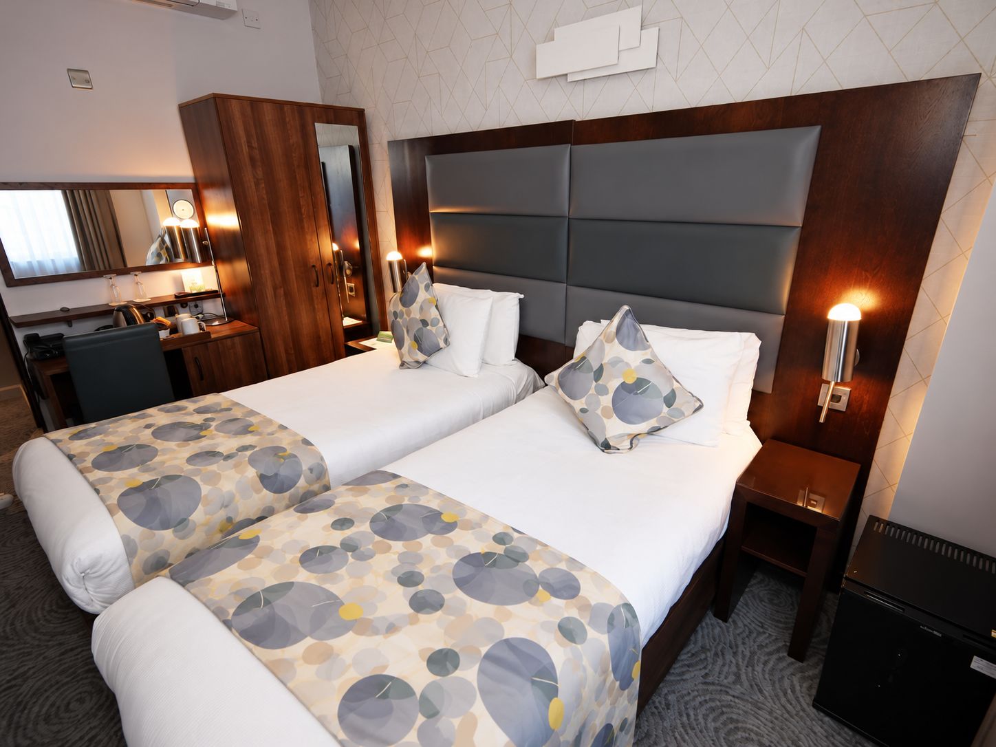 Habitación de hotel con dos camas, un escritorio, un espejo y un refrigerador.