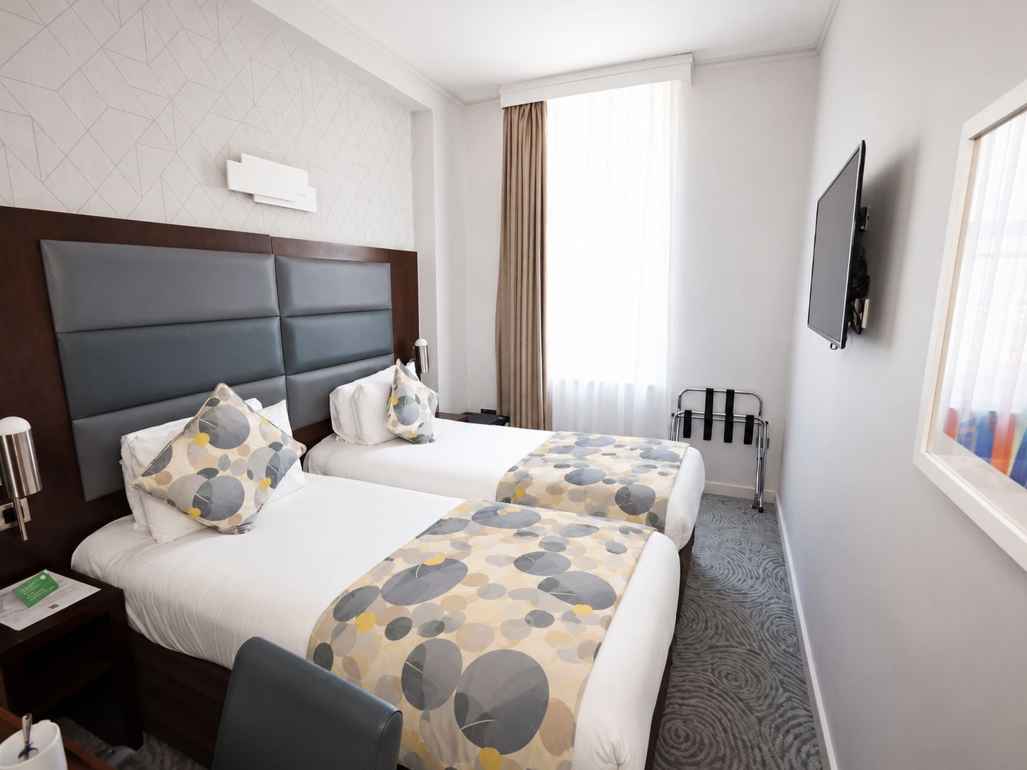 Ein Hotelzimmer mit zwei Betten, einem Flachbildfernseher, einem Fenster mit Vorhängen und einer Heizung.