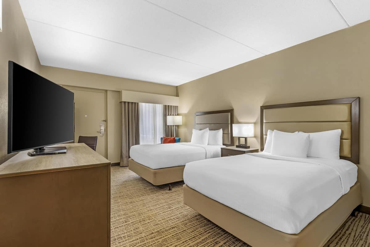 Une chambre d’hôtel avec deux lits, un bureau, une télévision et une fenêtre avec des rideaux.