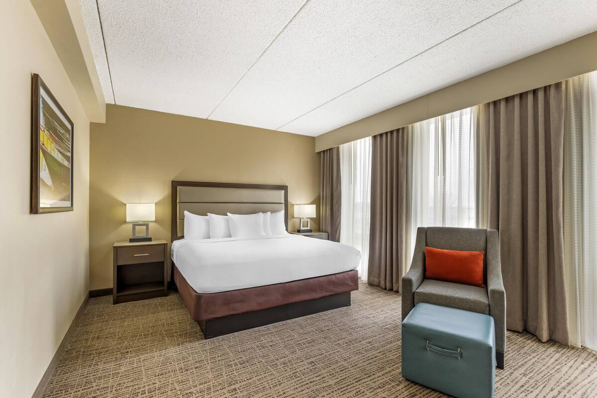 Une chambre d’hôtel avec un grand lit, une chaise, une table de chevet et une valise.