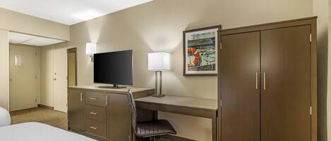 Een hotelkamer met een bed, bureau, stoel, televisie, kledingkast en kunstwerk aan de muur.