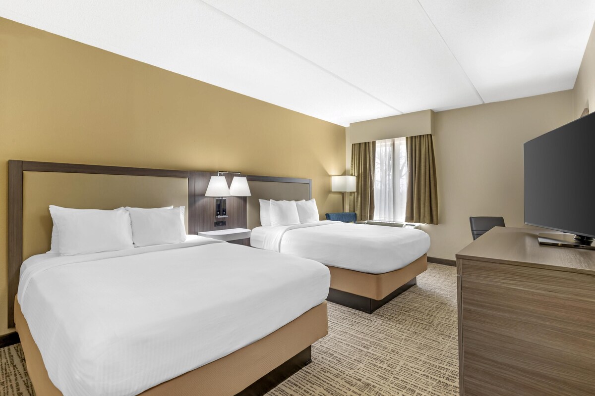A hotel room with two beds, a desk, a television, and a window with curtains.