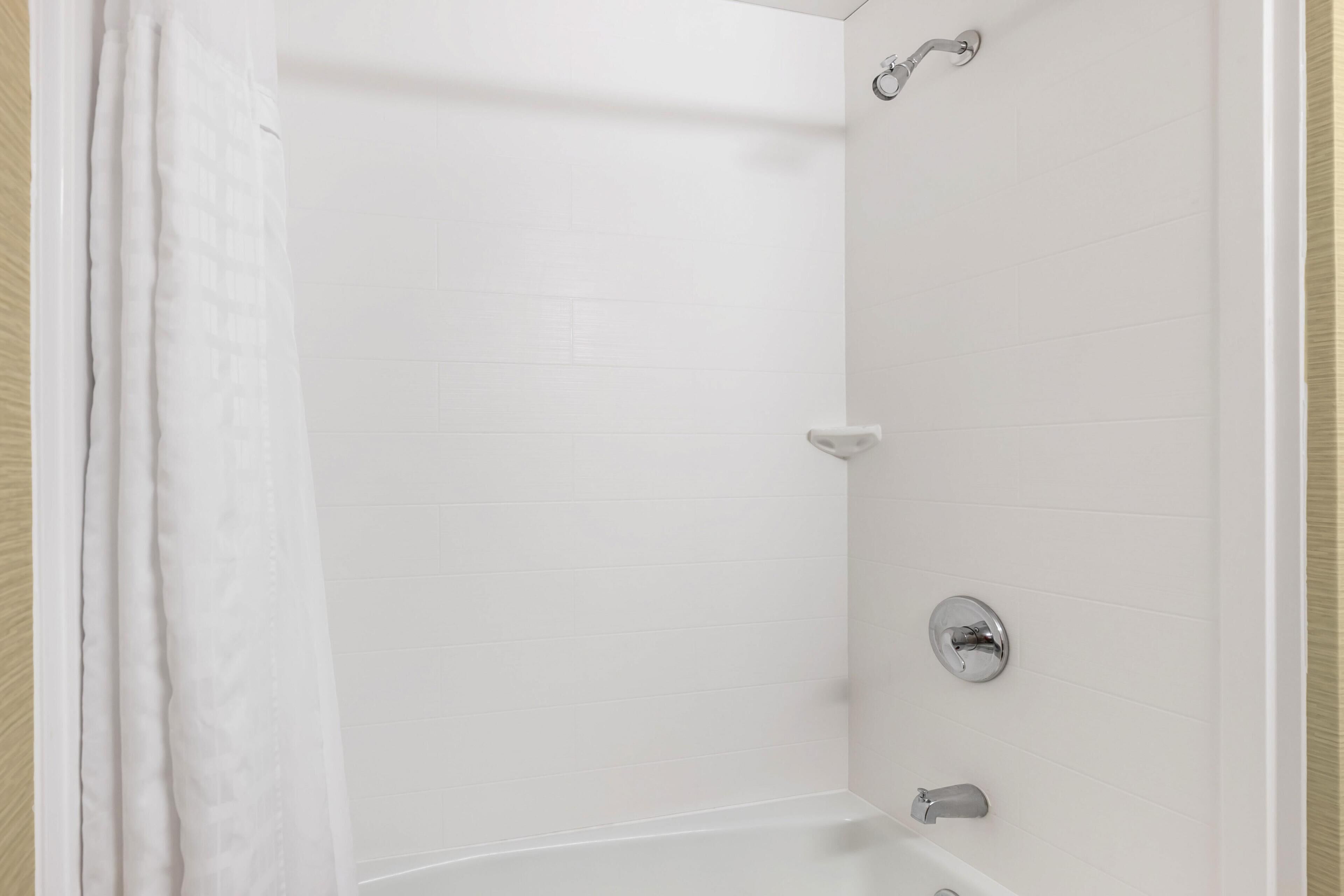A corner of a bathroom with white tiled walls, a shower curtain, and a bathtub with a faucet.