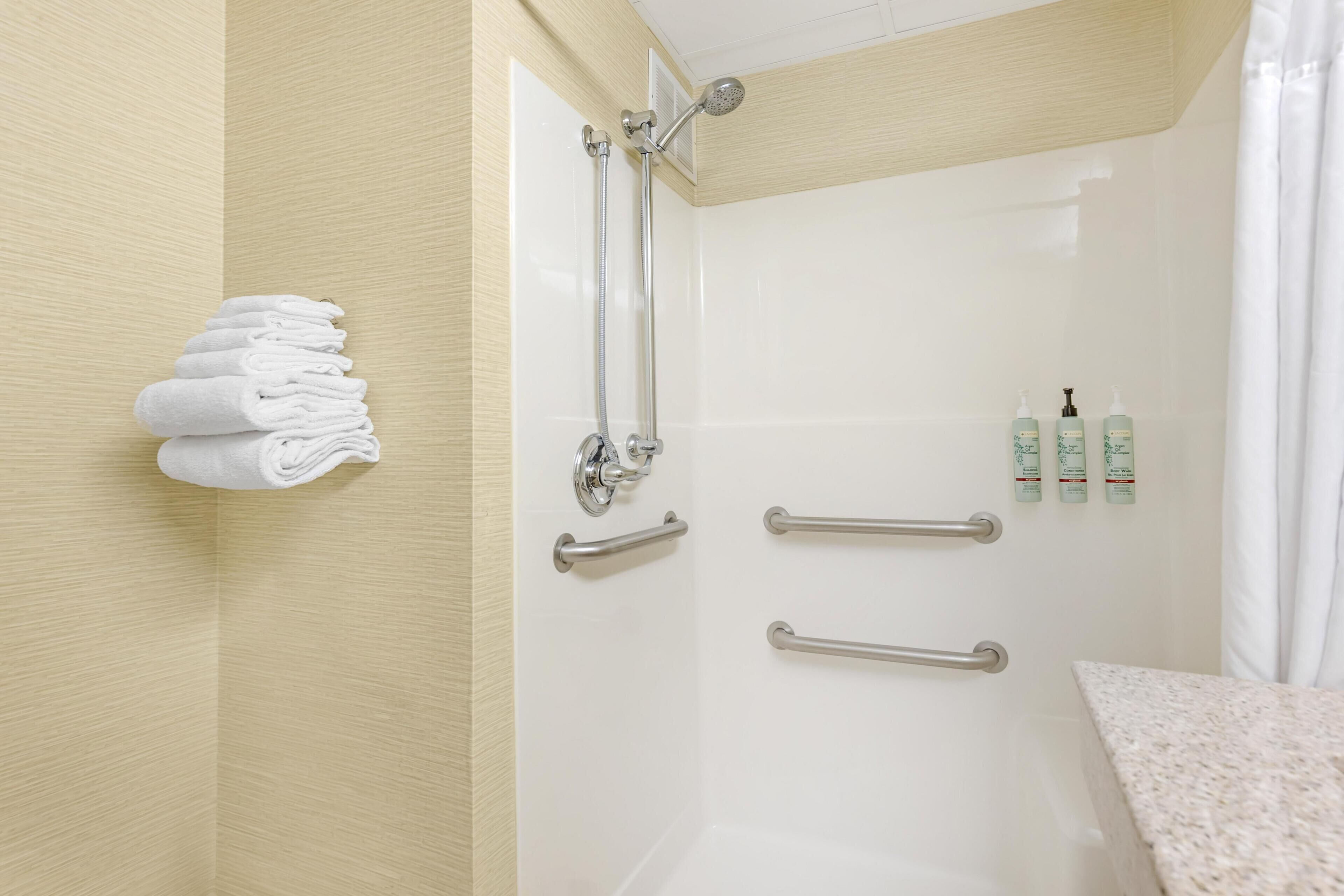 A shower with a glass door, a towel rack with folded towels, and two handrails.