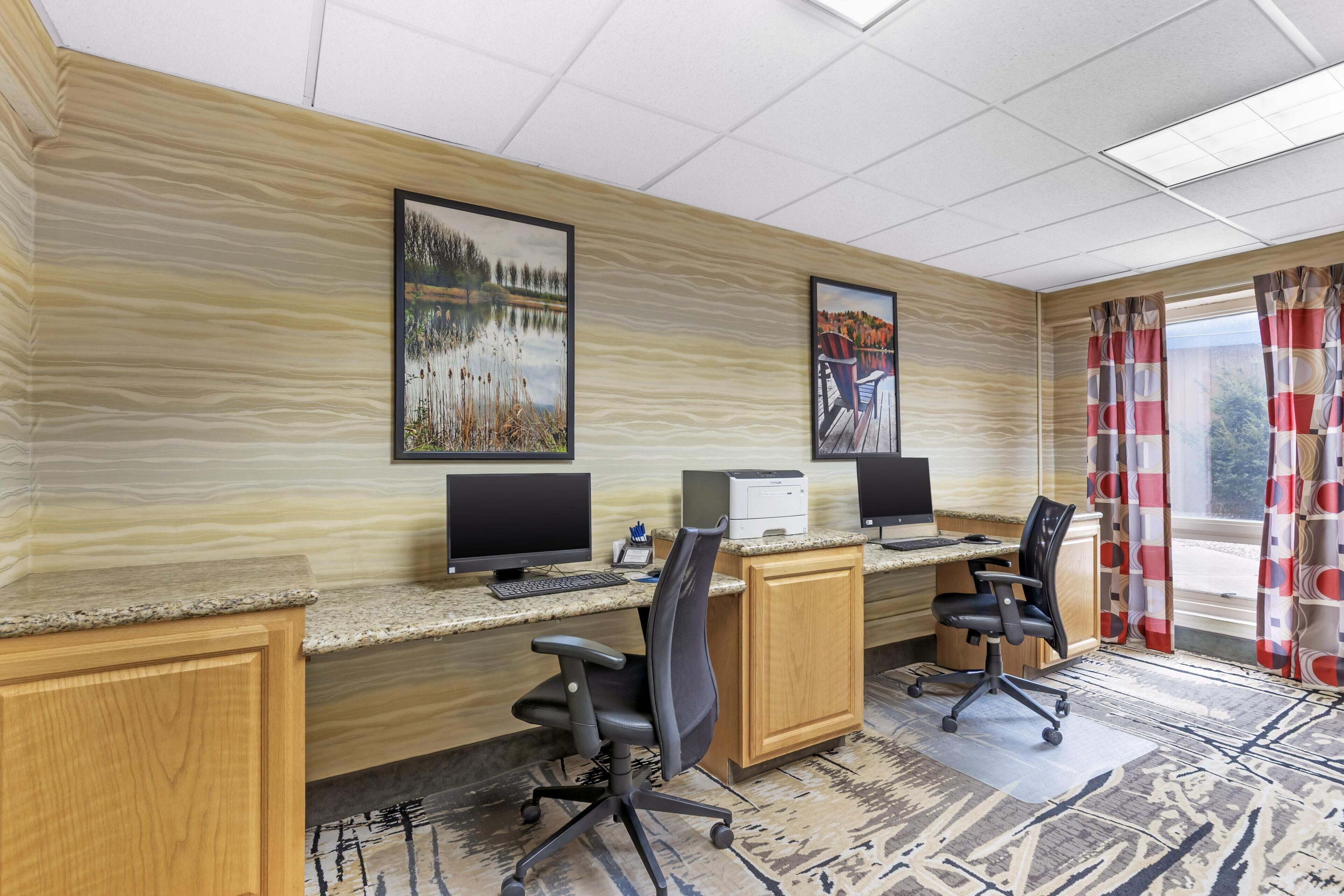 Une chambre d’hôtel avec un bureau en bois, deux écrans d’ordinateur, deux chaises de bureau et une grande fenêtre avec des rideaux rouges.