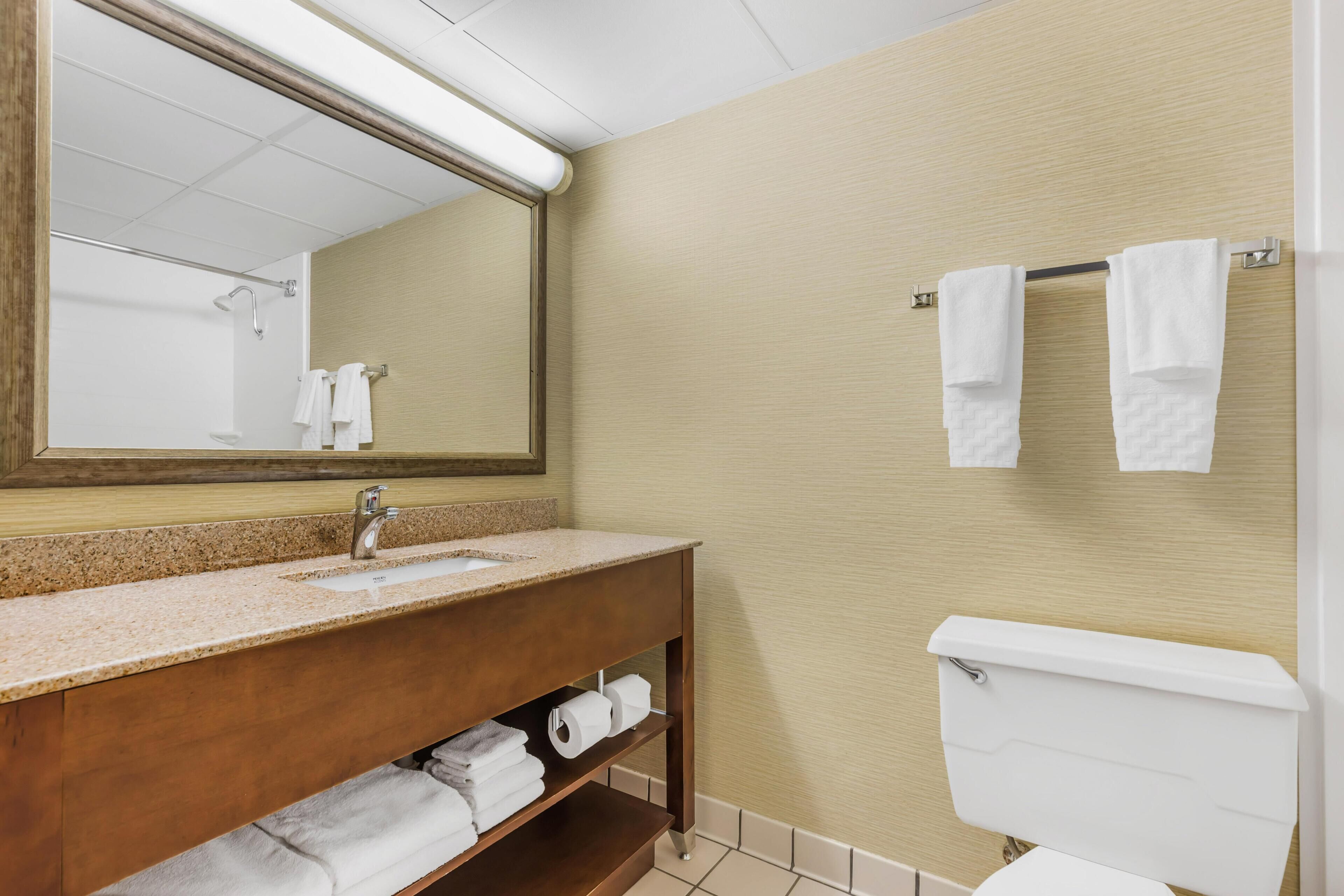 A bathroom with a sink, mirror, towel rack, toilet, and shelves with towels.
