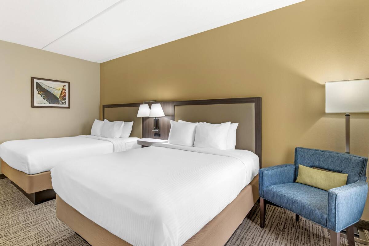 Une chambre d’hôtel avec deux lits, une table de chevet, une lampe, une chaise et un tableau encadré au mur.