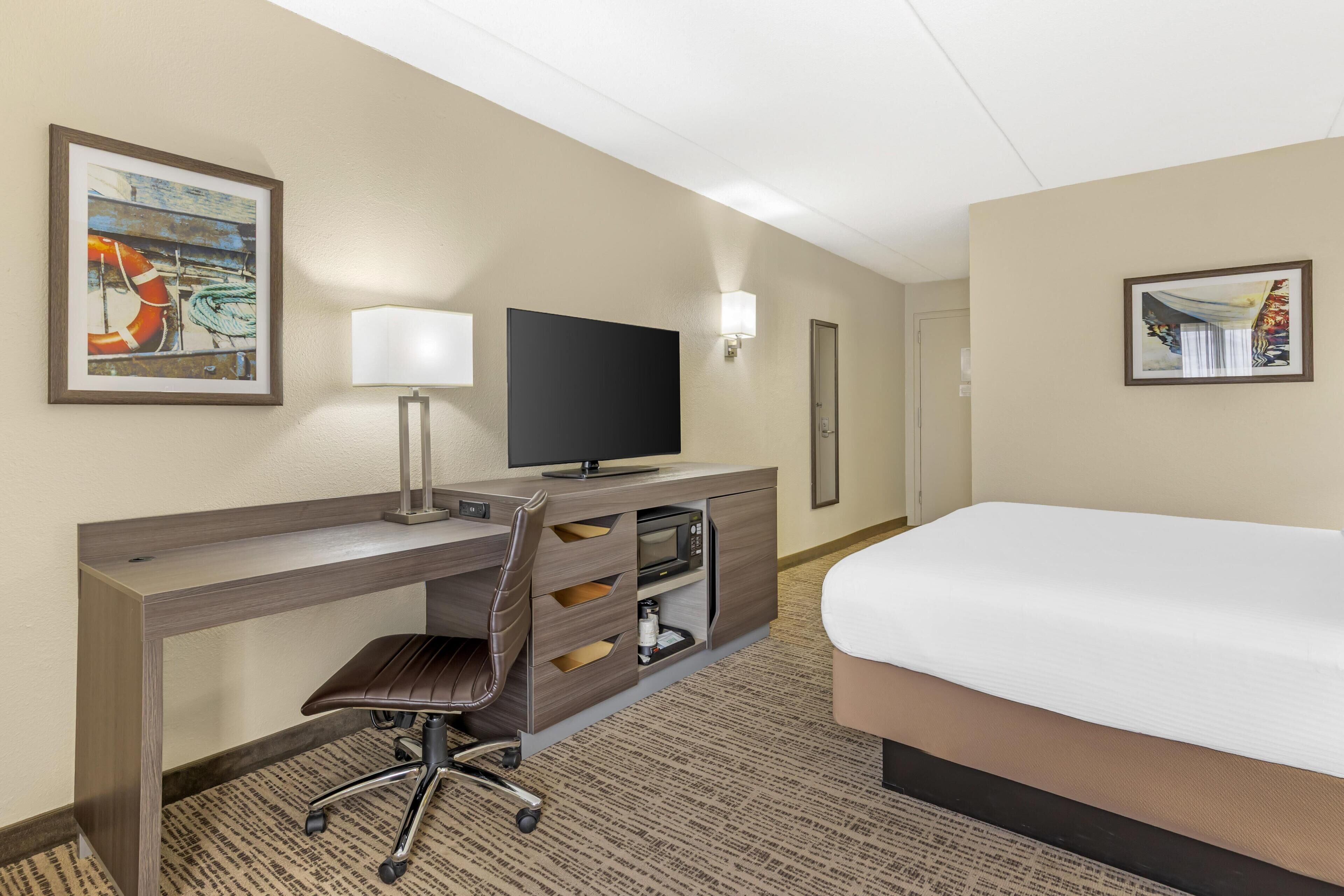 A hotel room with a bed, desk, chair, television, and artwork on the walls.