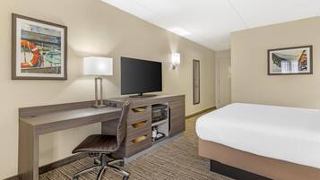 A hotel room with a bed, desk, chair, television, and artwork on the walls.