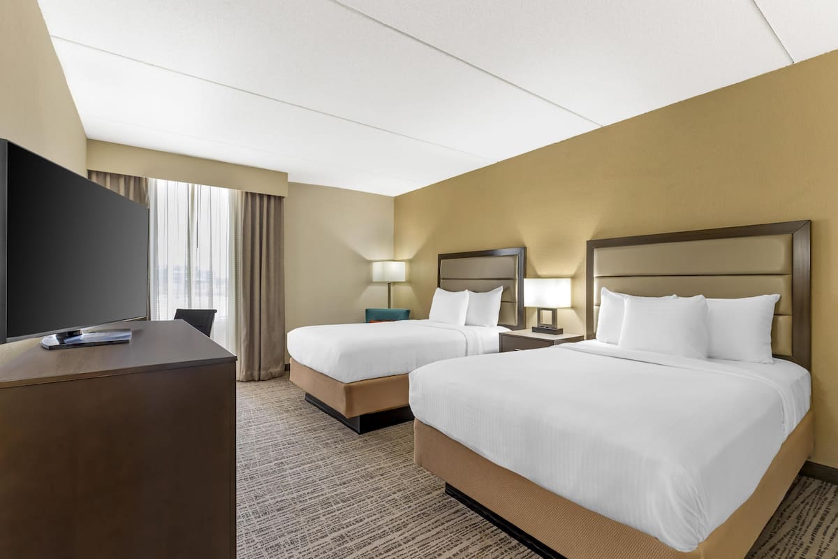 Une chambre d’hôtel avec deux lits, un bureau, une télévision et une fenêtre avec des rideaux.