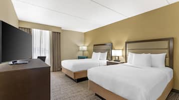 A hotel room with two beds, a desk, a TV, and a window with curtains.