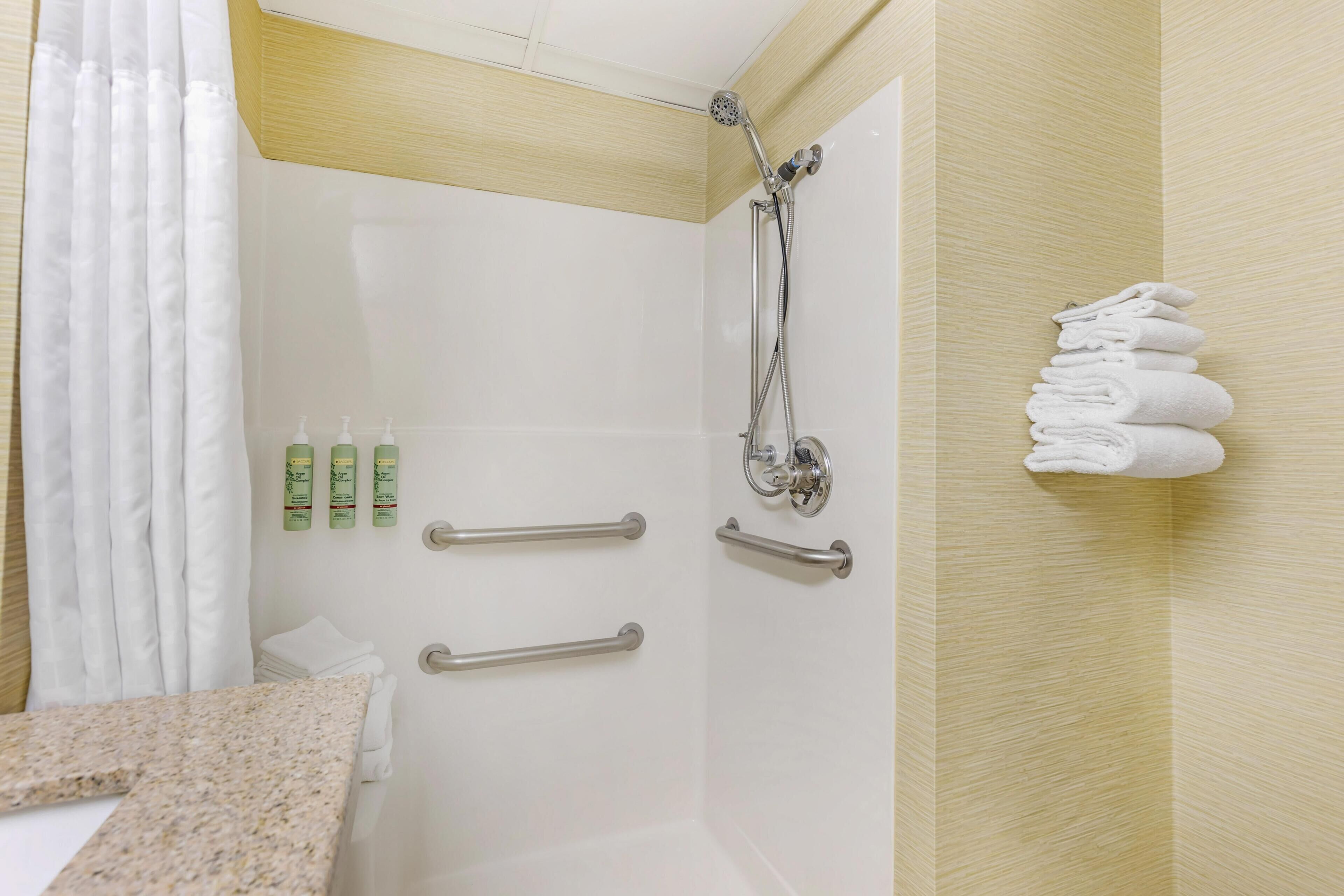 Une salle de bain équipée d’une douche, de barres d’appui, d’un porte-serviettes et d’articles de toilette.