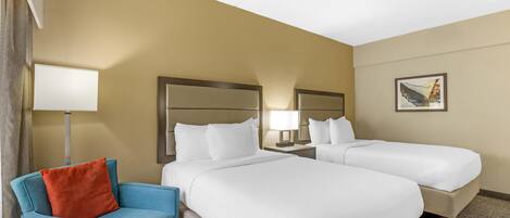 A hotel room with two beds, a blue chair, a lamp, and a painting on the wall.