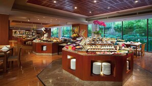 A buffet area with multiple serving stations, a chef, and a large window offering a view of greenery. - XI’AN DAJING CASTLE HOTEL (Xi'an)