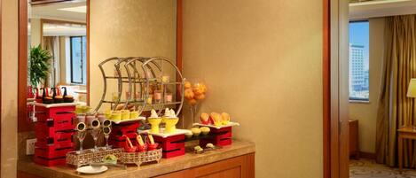 Une chambre d’hôtel avec un buffet de petit-déjeuner comprenant un panier de fruits, un coin café et un présentoir à verres.