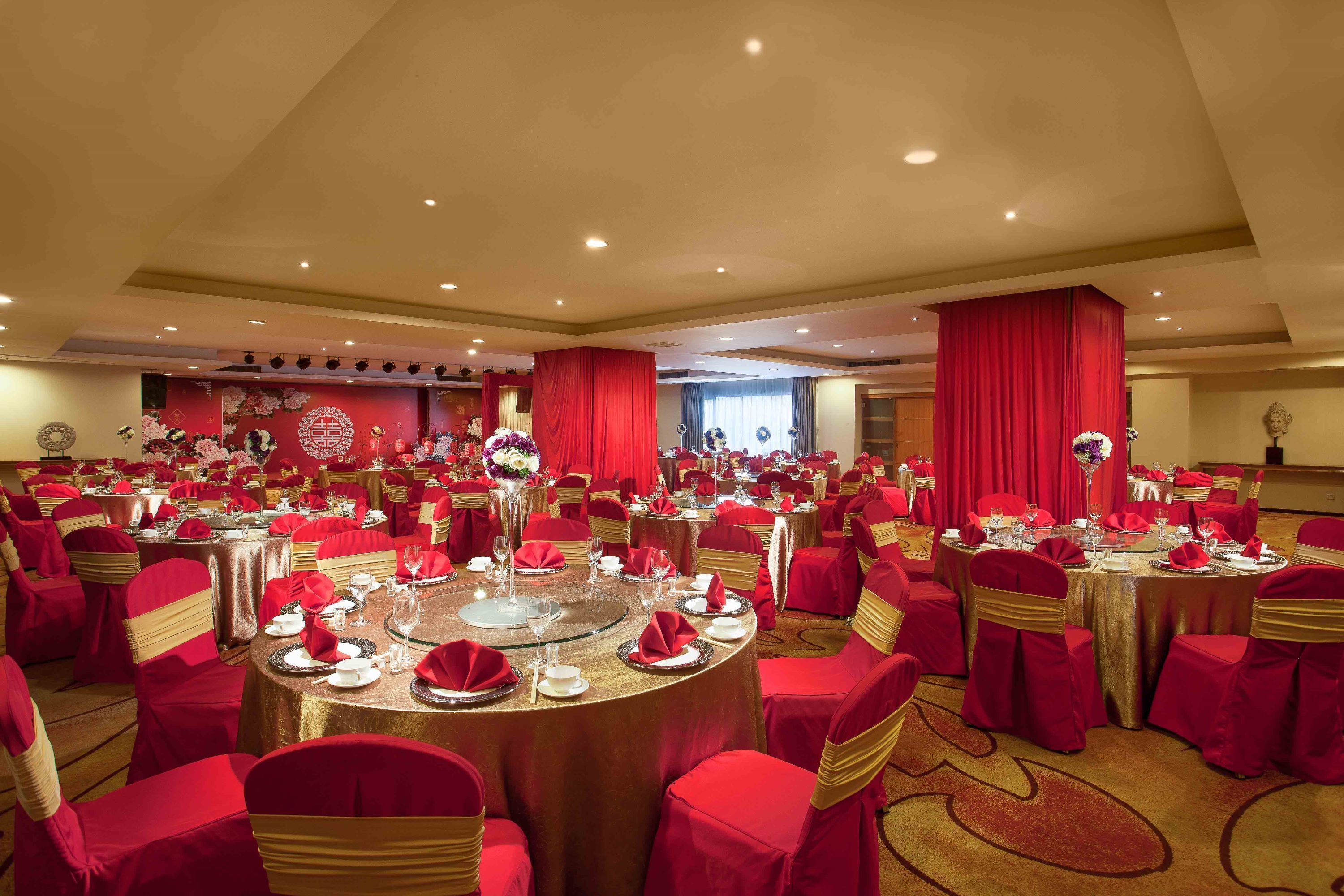 A banquet hall with round tables, red chairs, and gold sashes.
