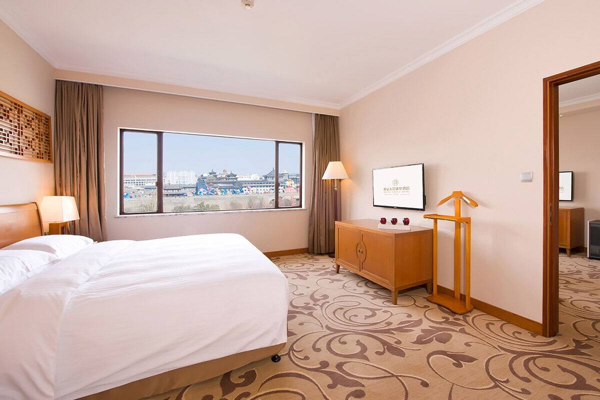 Een hotelkamer met een groot bed, een bureau, een stoel, een televisie en uitzicht op een stadsgezicht.