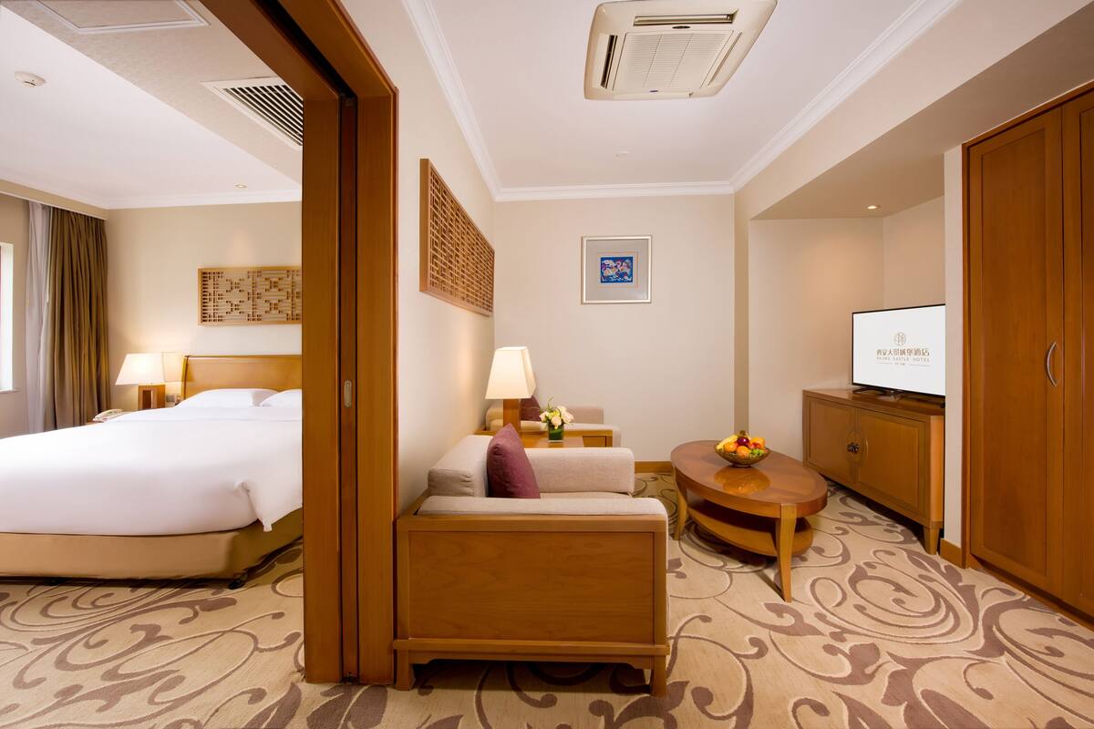 Een hotelkamer met een bed, een bank, een bureau met lamp, een televisie en een kledingkast.