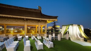 A traditional building with a tiled roof and a covered outdoor area with rows of white chairs and a green carpet. - XI’AN DAJING CASTLE HOTEL (Xi'an)