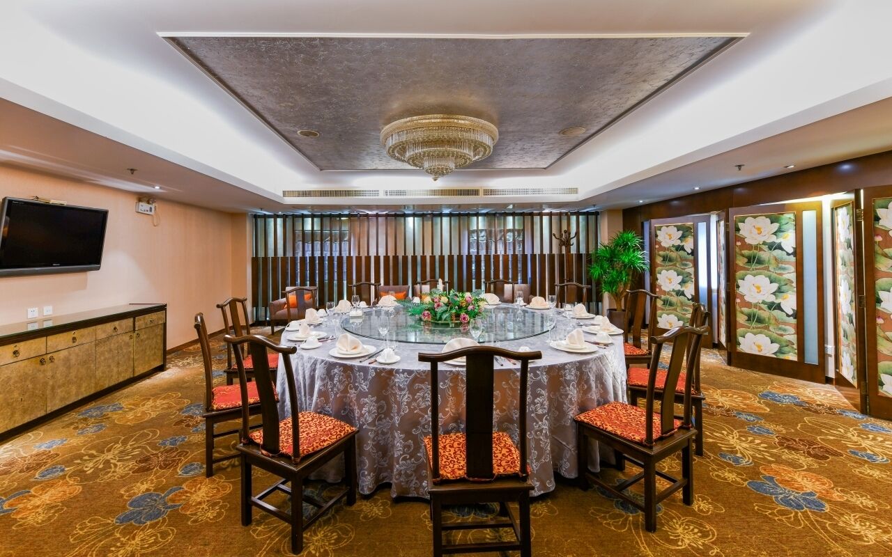 A round dining table with chairs, a chandelier, and a television on the wall.