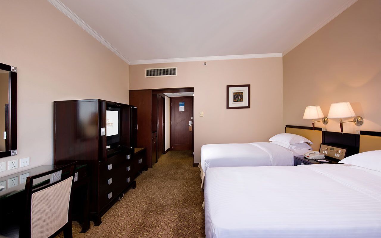A hotel room with two beds, a desk with a chair, a dresser, a television, and a framed picture on the wall.