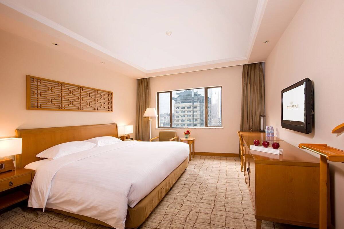 Een hotelkamer met een groot bed, een bureau, een stoel, een televisie en een raam met uitzicht op de stad.