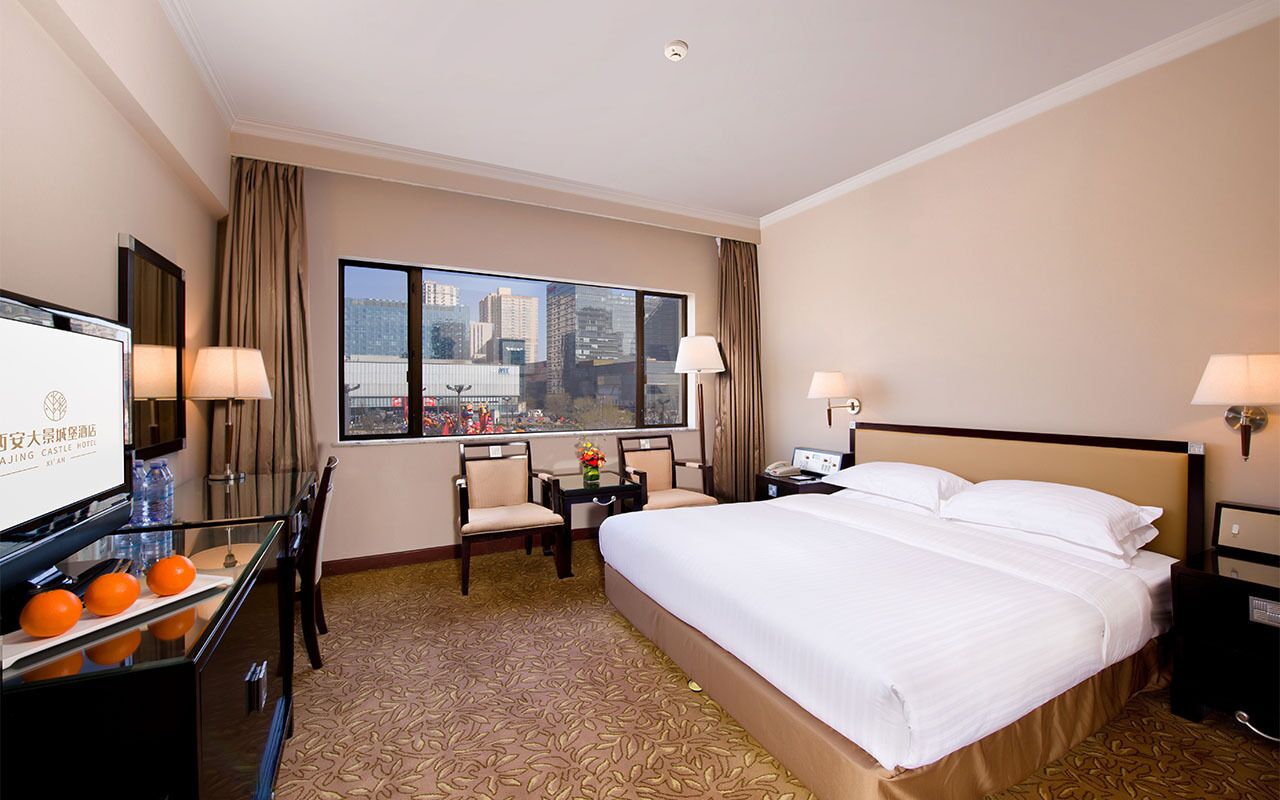 Habitación de hotel con una cama grande, un escritorio con silla, televisor y vista a la ciudad.