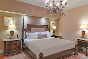 Une chambre d’hôtel avec un grand lit, deux tables de chevet avec des lampes, un lustre et des œuvres d’art encadrées accrochées aux murs.