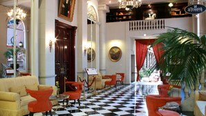 A lobby with a checkered floor, red and beige chairs, a large chandelier, and a portrait on the wall.