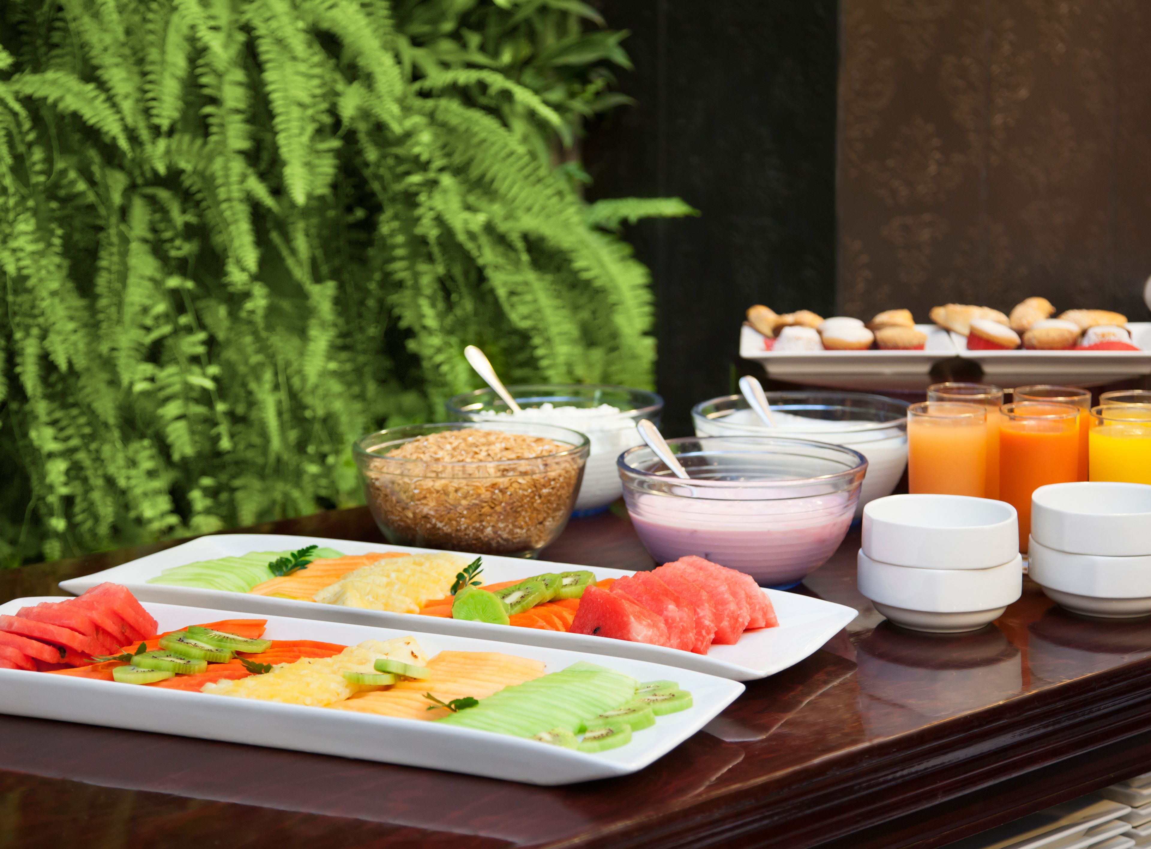 A breakfast buffet with various fruits, cereals, and beverages on a wooden table.