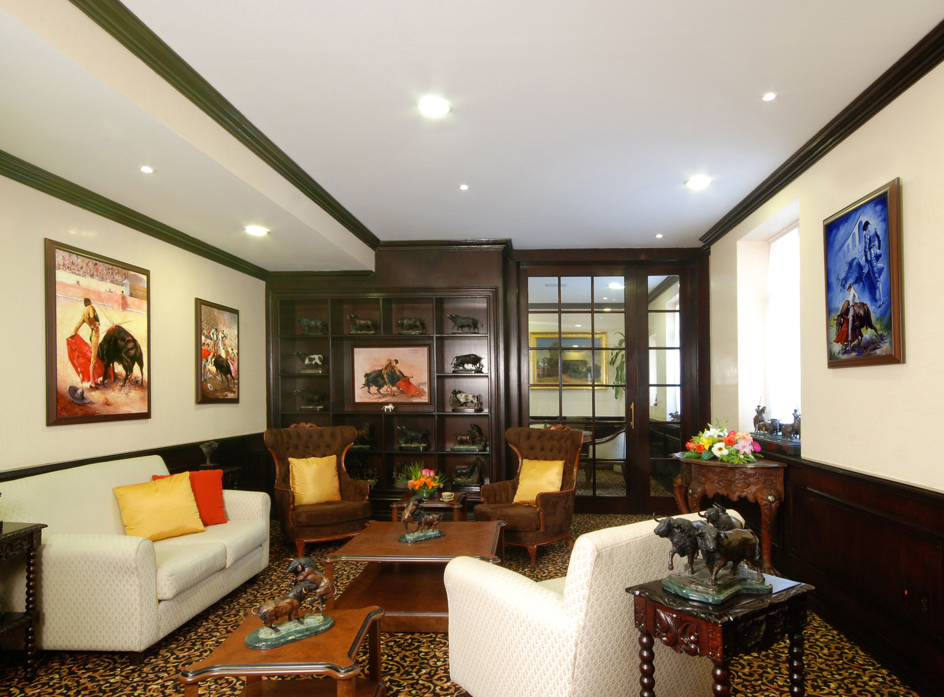 A spacious living room with a sofa, armchairs, and a coffee table. There are framed pictures on the walls and a bookshelf filled with books and decorative items.