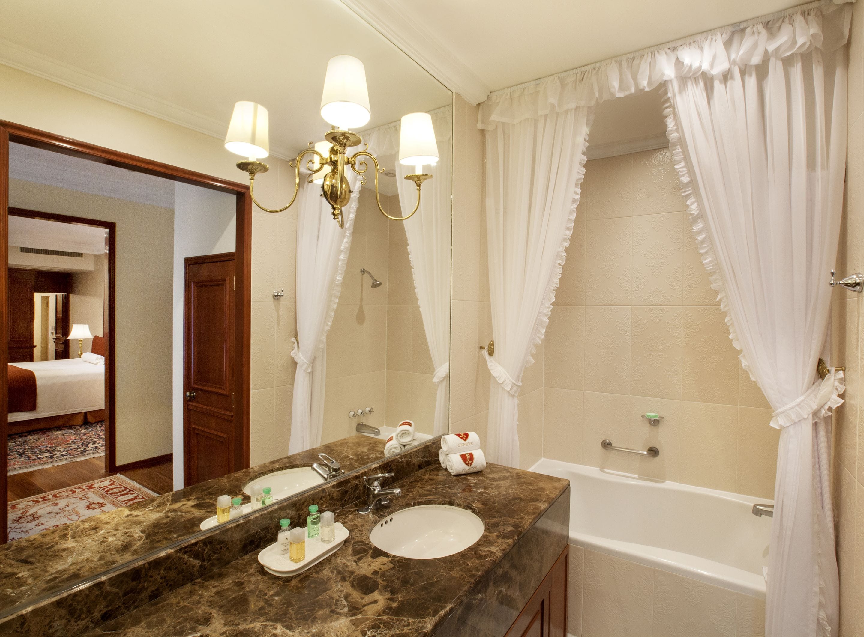 A bathroom with a marble sink, a bathtub, and a shower with white curtains.