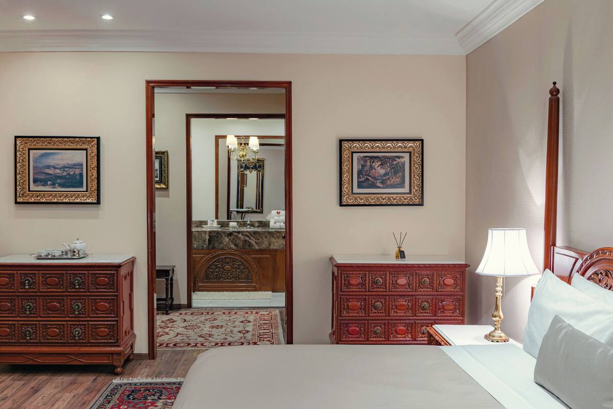 Une chambre d’hôtel avec un lit, deux commodes en bois, une table de chevet, une lampe et un miroir.