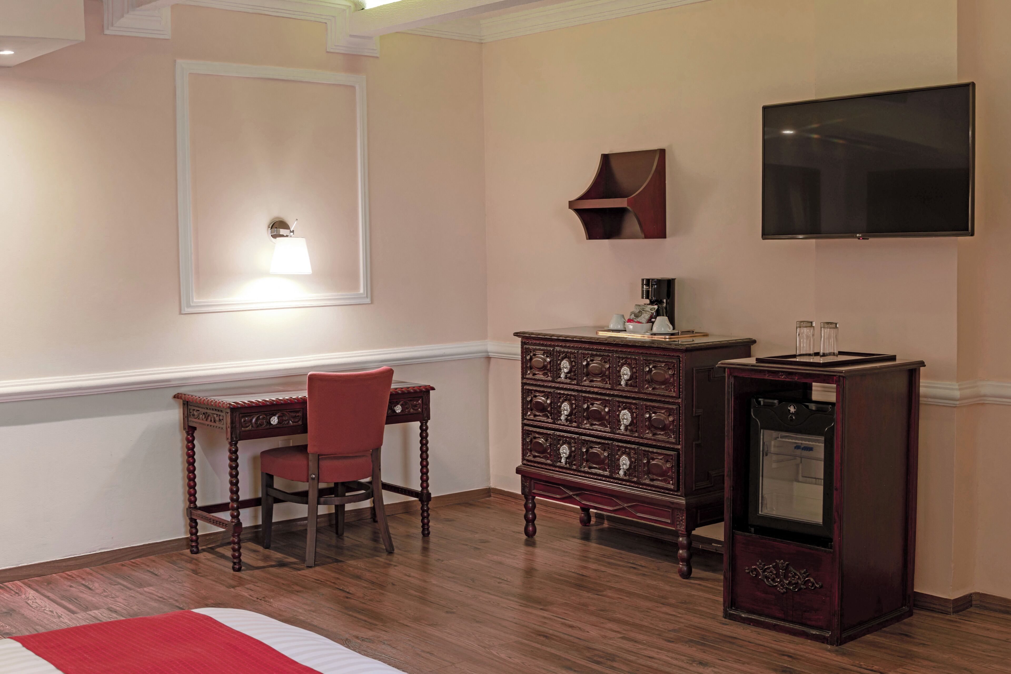 A room with a wooden desk, a chair, a dresser, a television, and a wall-mounted shelf.