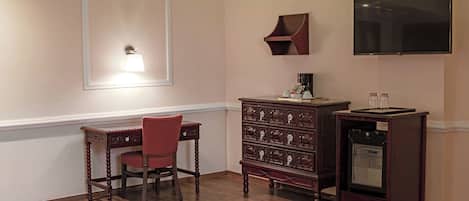 A room with a wooden desk, a chair, a dresser, a television, and a wall-mounted shelf.
