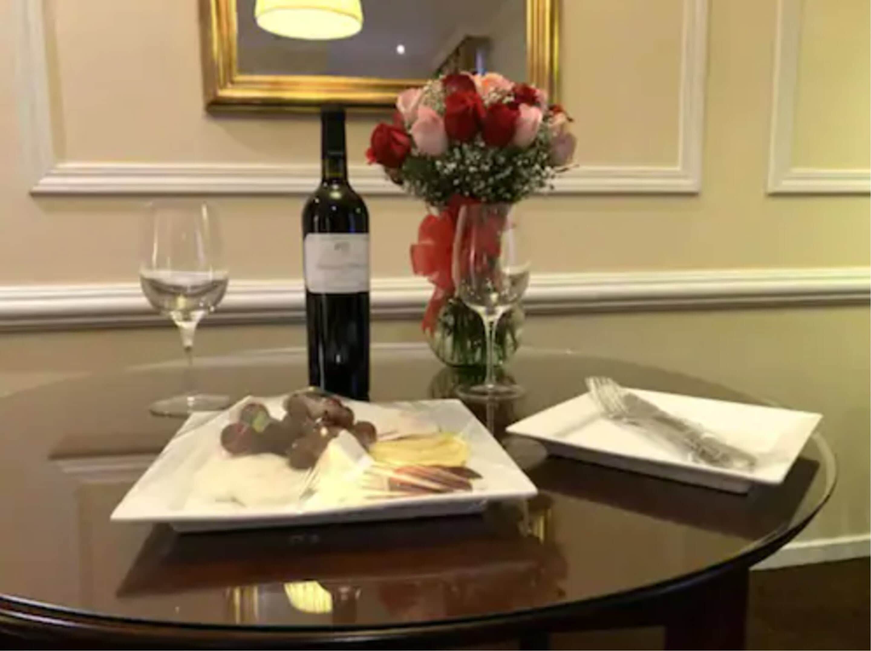 Una mesa redonda con una botella de vino, una copa de vino, un plato de comida, un florero con flores y una servilleta.