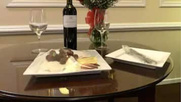 Una mesa redonda con una botella de vino, una copa de vino, un plato de comida, un florero con flores y una servilleta.