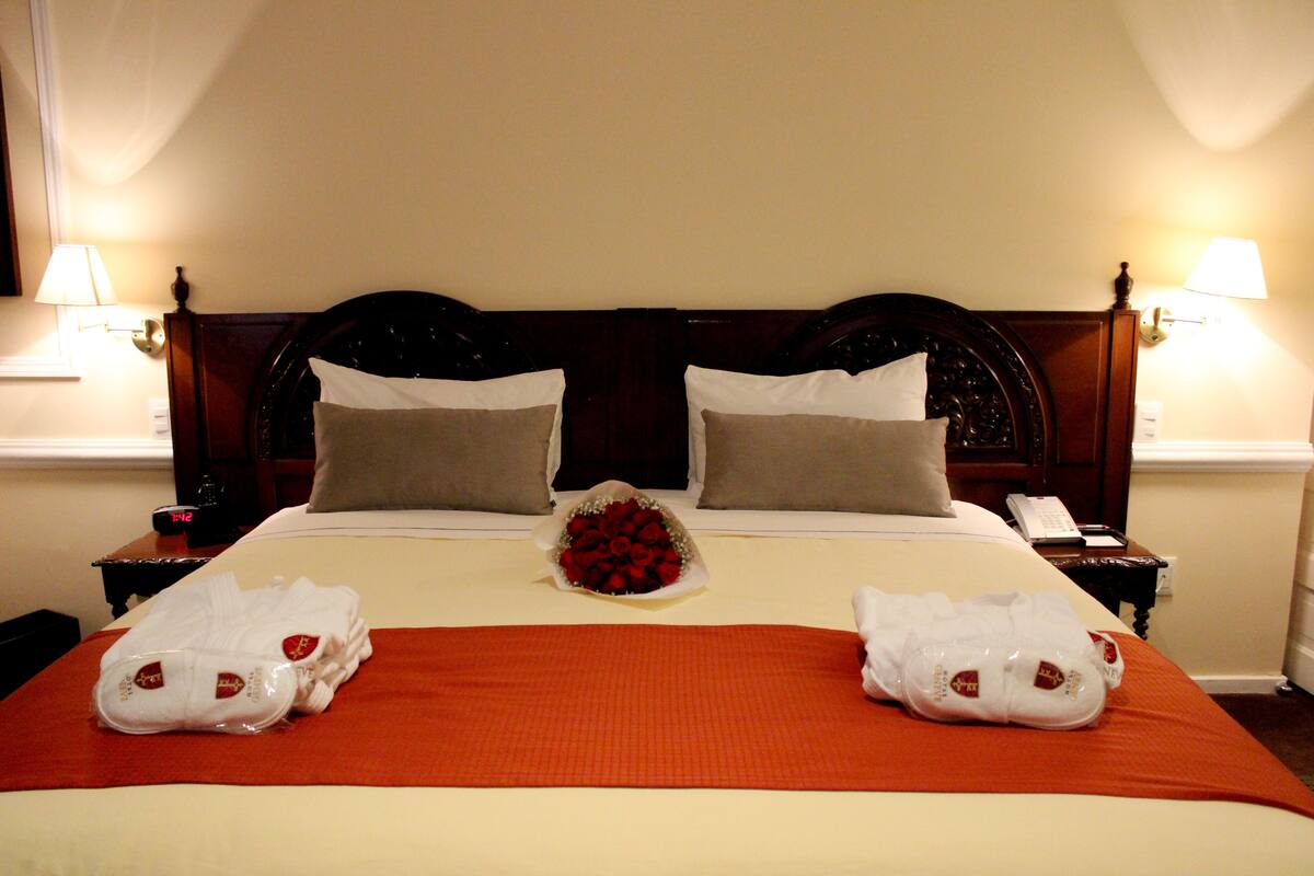 Une chambre d’hôtel avec un grand lit, deux tables de chevet, un bouquet de roses rouges et deux serviettes sur le lit.