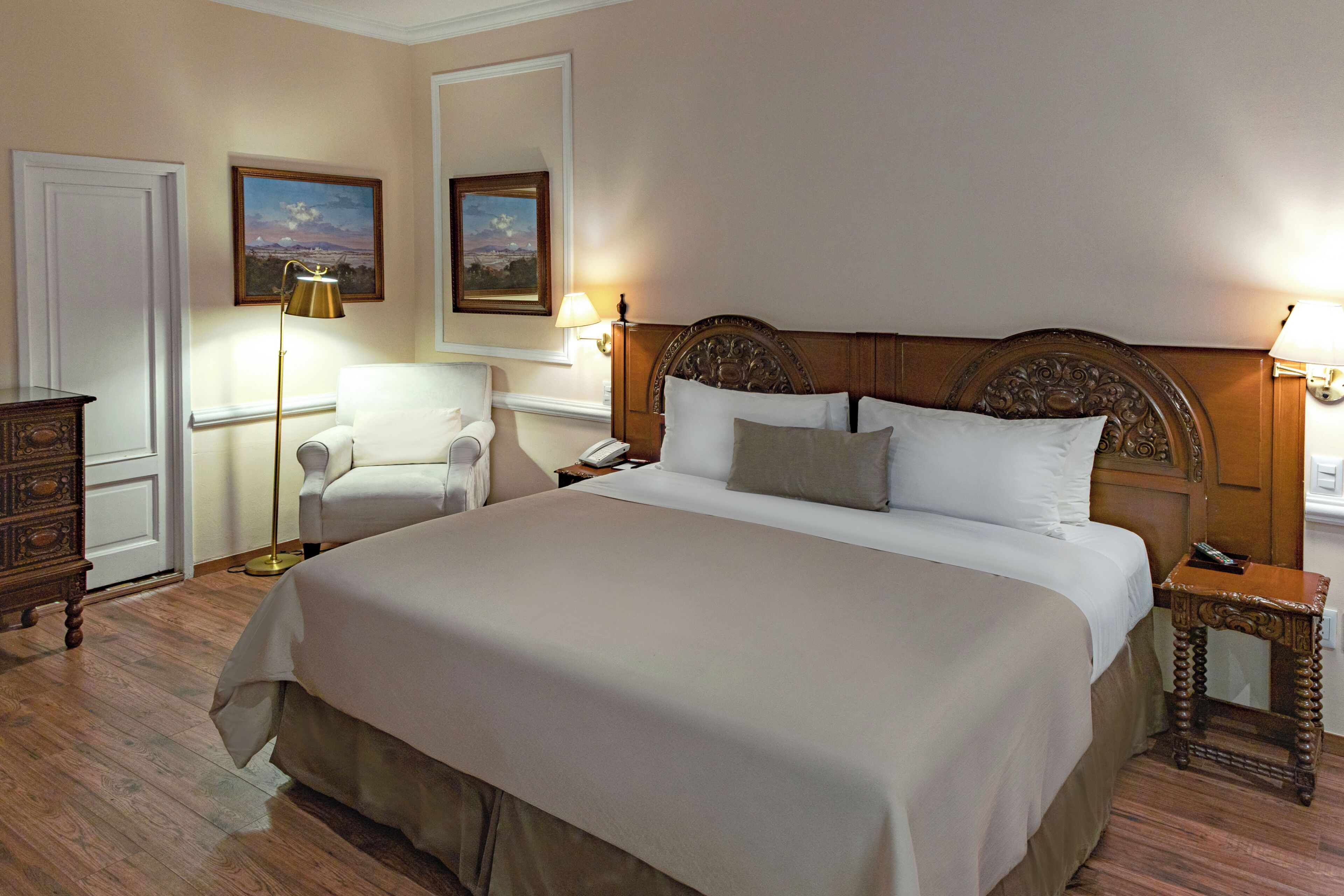 A hotel room with a large bed, bedside tables, a desk, a chair, and a dresser.