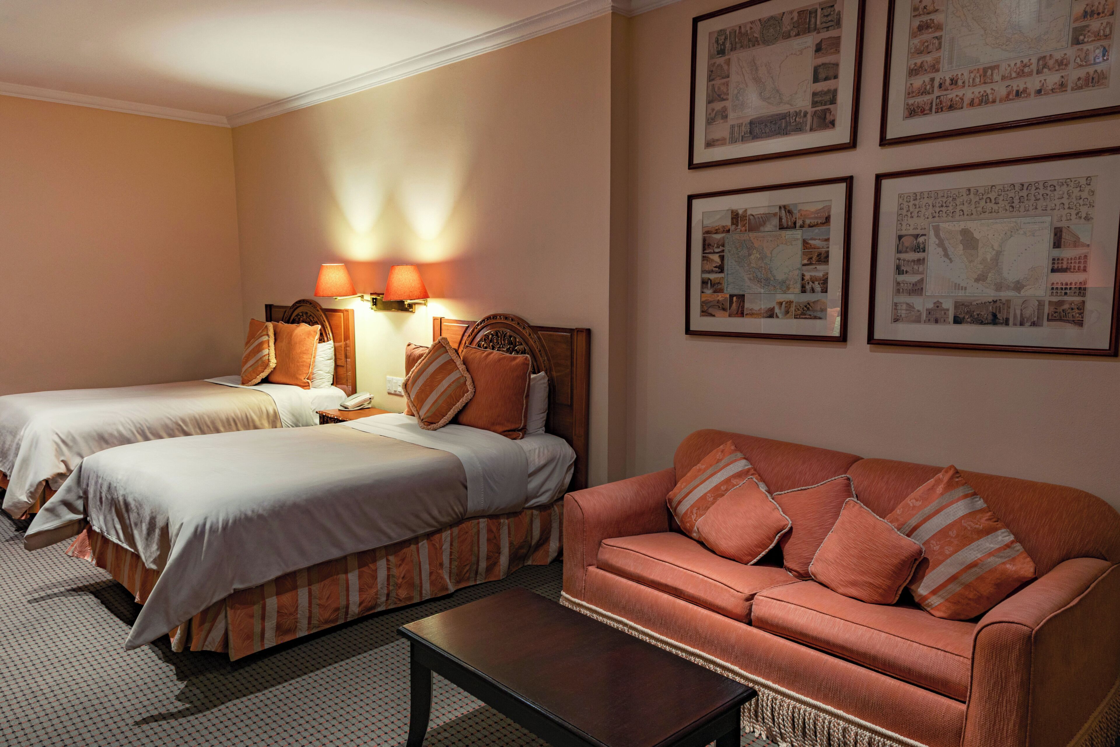 A hotel room with two beds, a sofa, a nightstand, and wall-mounted lamps.