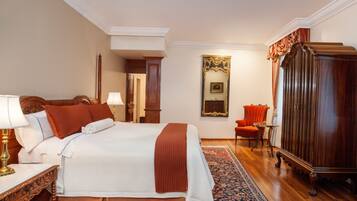 Habitación de hotel con una cama grande, un armario de madera, un sillón rojo y una alfombra estampada.