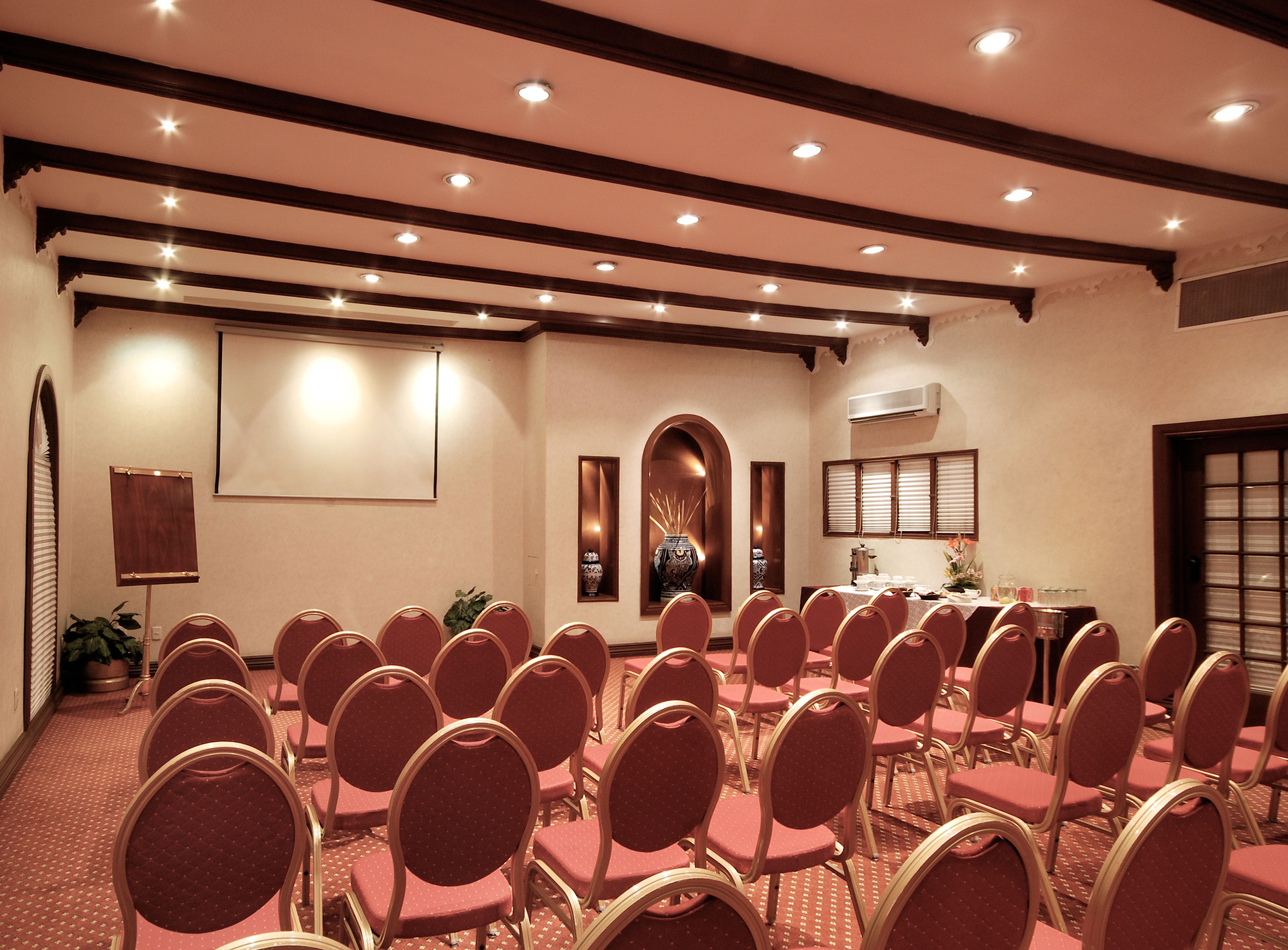 A conference room with rows of red chairs, a projector screen, and a large vase on a pedestal.