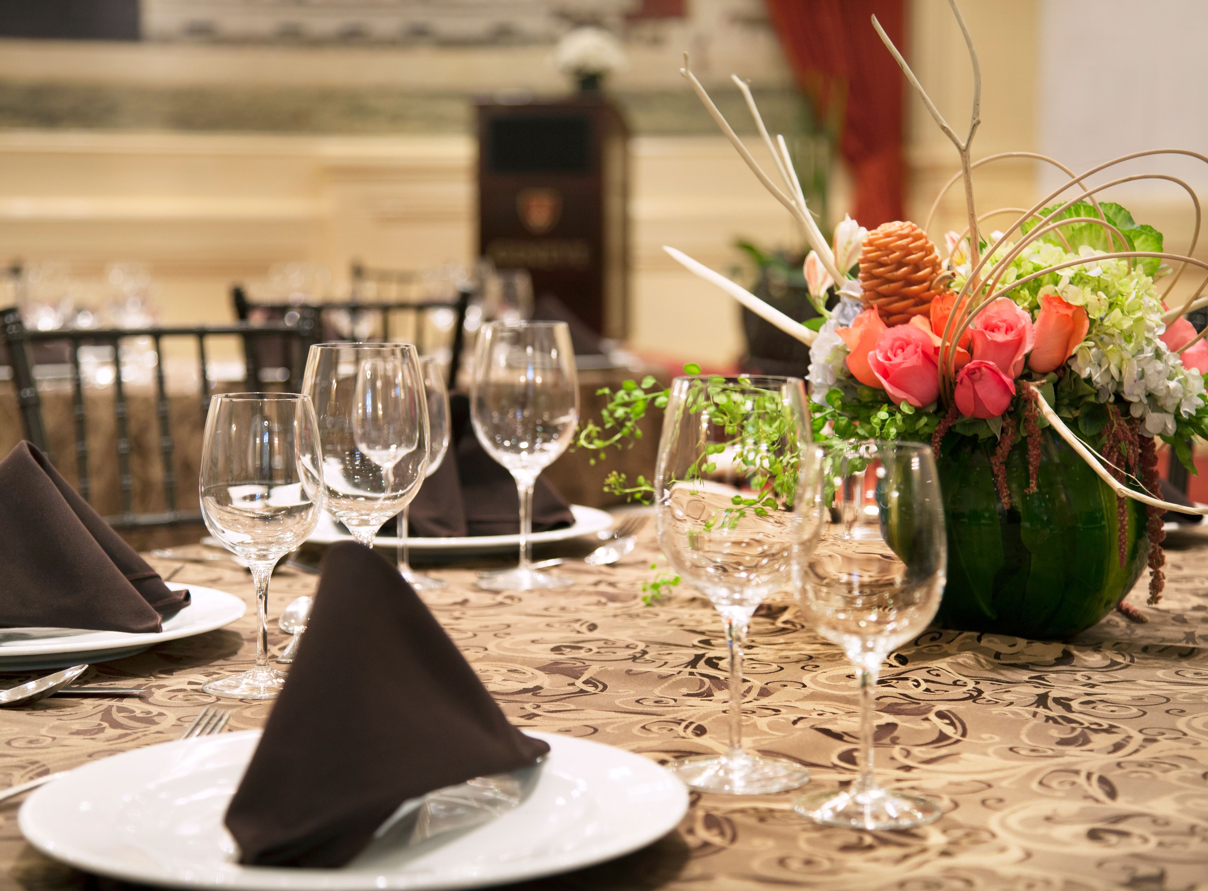 A dining table set with multiple wine glasses, plates, and a centerpiece with flowers and greenery.