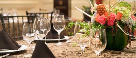 A dining table set with multiple wine glasses, plates, and a centerpiece with flowers and greenery.