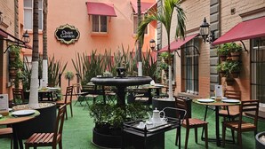 An outdoor café area with tables and chairs, a central fountain, and potted plants.