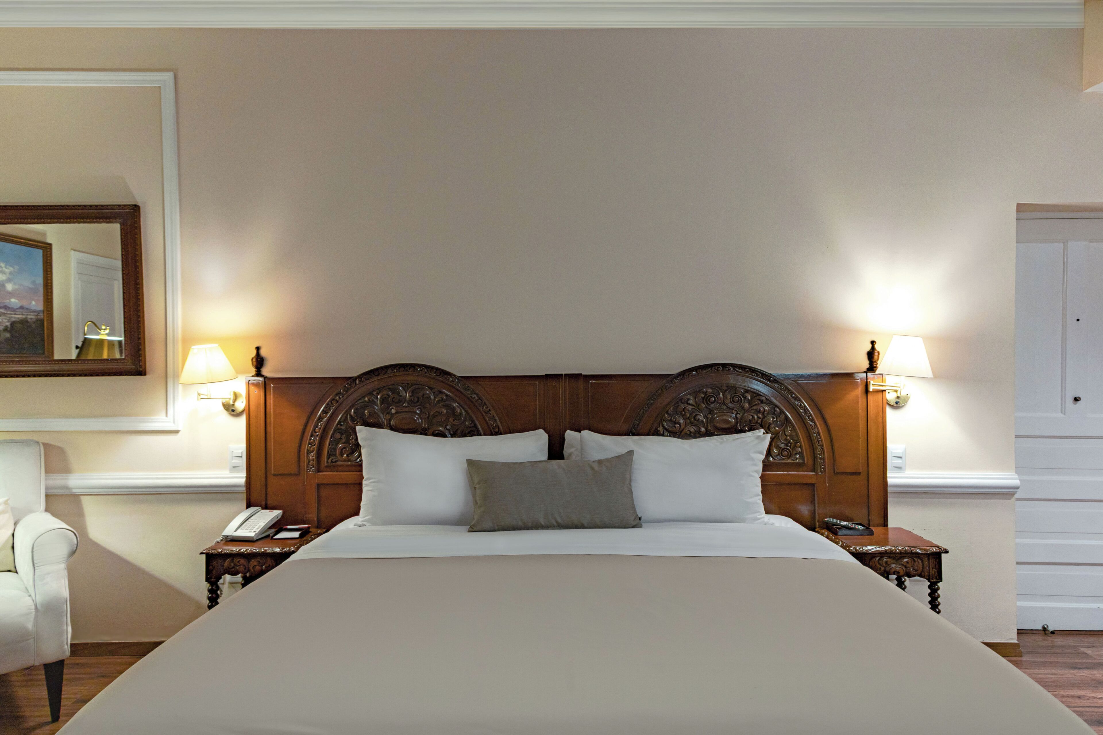 Una cama grande con cabecera de madera, dos lámparas de noche y una mesita de noche con teléfono.