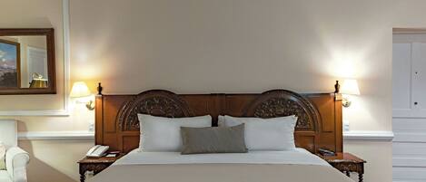 Una cama grande con cabecera de madera, dos lámparas de noche y una mesita de noche con teléfono.